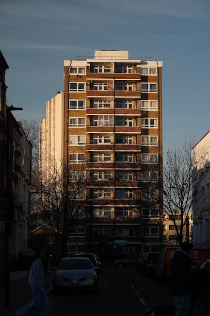 Aerial view of a residential area showing a mix of houses, low-rise apartments, and two tall, multi-storey apartment buildings positioned centrally within the scene. The foreground features rows of te